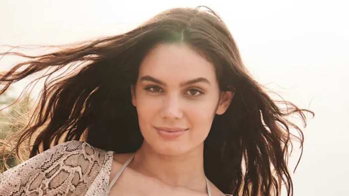 Anne de Paula poses for the camera, wearing a snakeskin-printed top and her brown hair down.